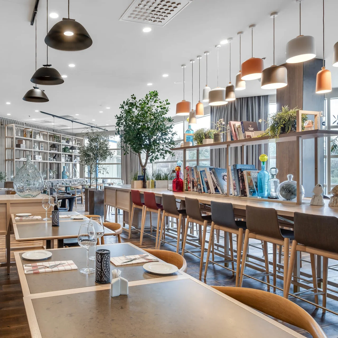 A modern, well-lit dining area with pendant lights, a bookshelf, and a vibrant wall print. The furniture is stylish and the space is inviting.