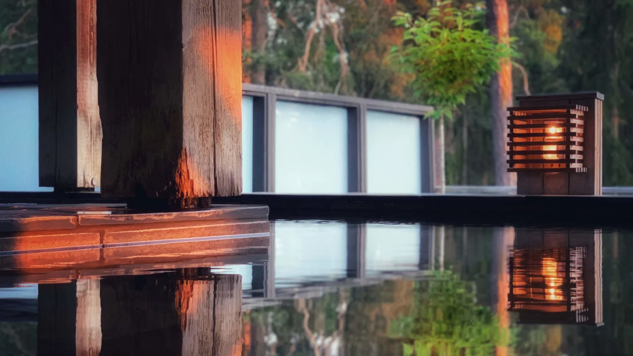 En trælygte reflekteres på en stille vandoverflade, med træer og en bygning i baggrunden.