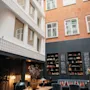 En indbydende hotellounge med et langt bord, komfortable siddepladser, bogreoler og tavler, der viser forskellige drikkevarer. Tekst: enjoy.