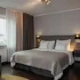 A cozy hotel room with a large bed, a comfortable armchair by the window, and warm lighting, inviting relaxation.