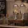 Glassdispensrar fyllda med vatten och citronskivor står på ett träställ vid en dryckesstation. På svarta tavlan står: "CARE 2025 HELP US REDUCE FOOD LOSS AND WASTE. For the people, for the planet."