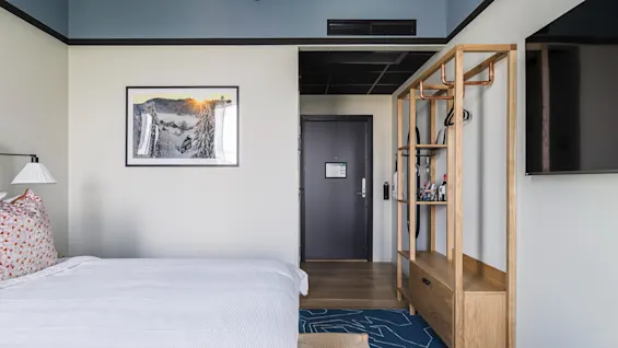 Et moderne hotelværelse på Hernö Gin Hotel med en komfortabel seng, et vinterlandskabskunstværk og et åbent træskab.