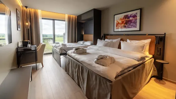 Ett välupplyst modernt hotellrum med två sängar, konst på väggen och utsikt över grönska utanför fönstret.