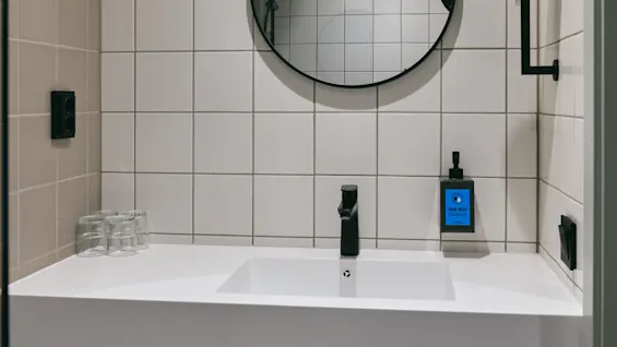 A modern bathroom vanity with a white sink, black faucet, round mirror, and neatly arranged towels and toiletries.