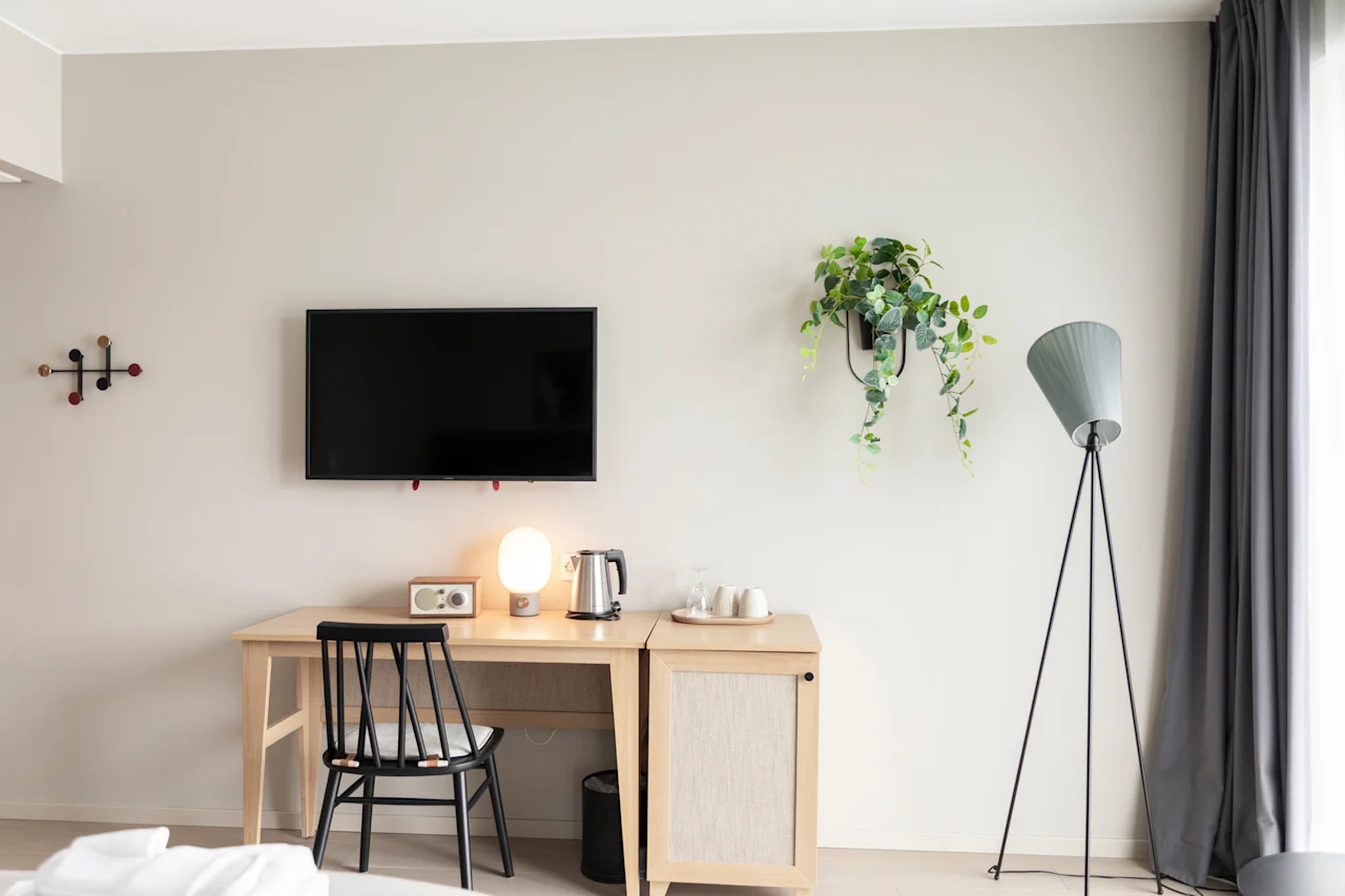 Moderni ja kutsuva huonejärjestely, jossa on puinen työpöytä, televisio ja mukava tuoli, täydennettynä kasvilla ja lampulla.