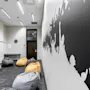 Bean bags rest on a carpeted floor in a minimalist room. A black silhouette mural decorates the wall, and a clock hangs above a small table. Text includes "RESPECT."