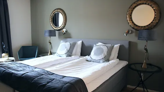 A cozy hotel room featuring a made double bed, two round mirrors, and soft bedside lighting.