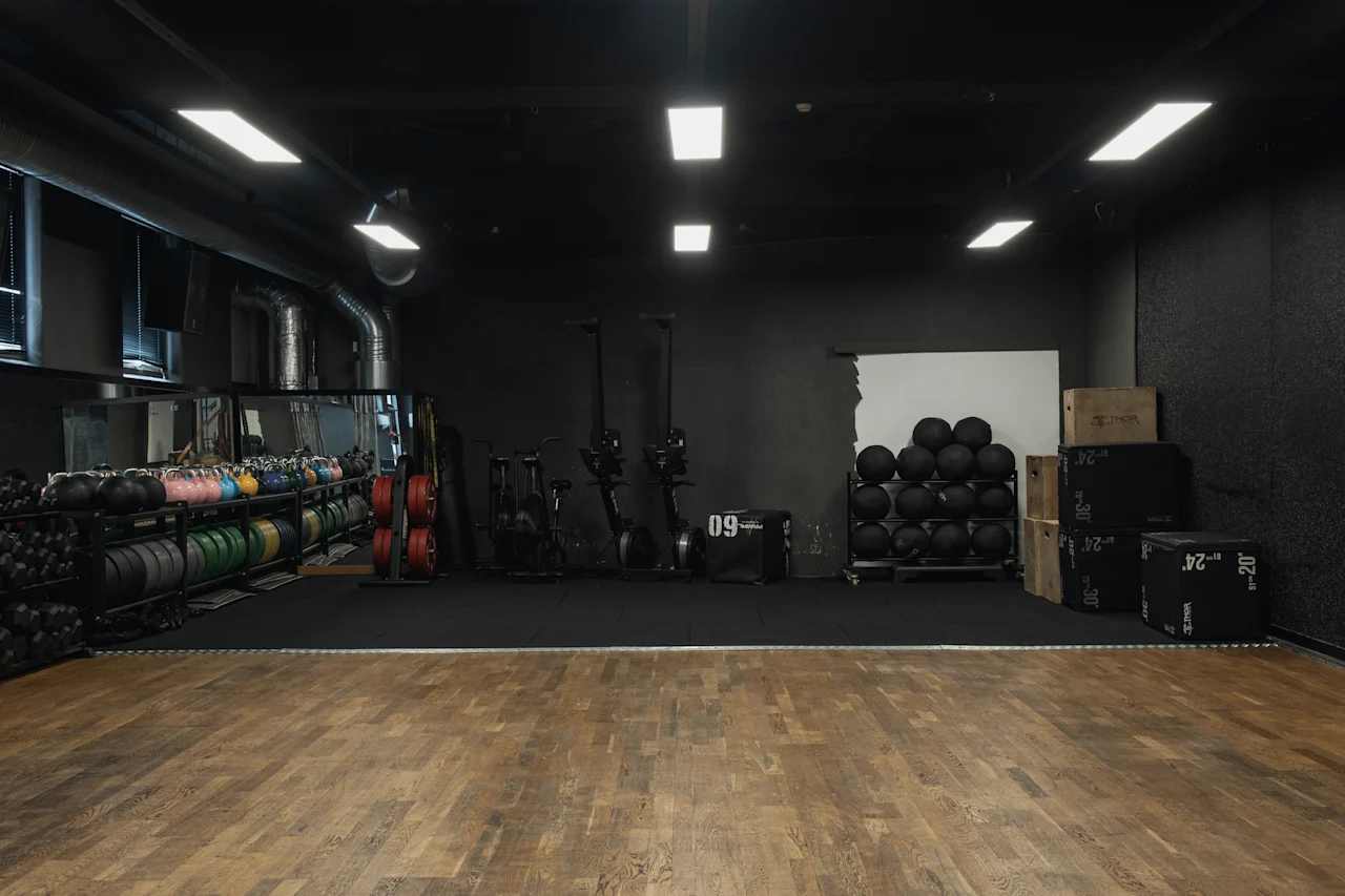 Et veludstyret fitnesscenter med vægte, træningsmaskiner og træ- og måttegulv. Synlig text: 09, 24, 30, 20.