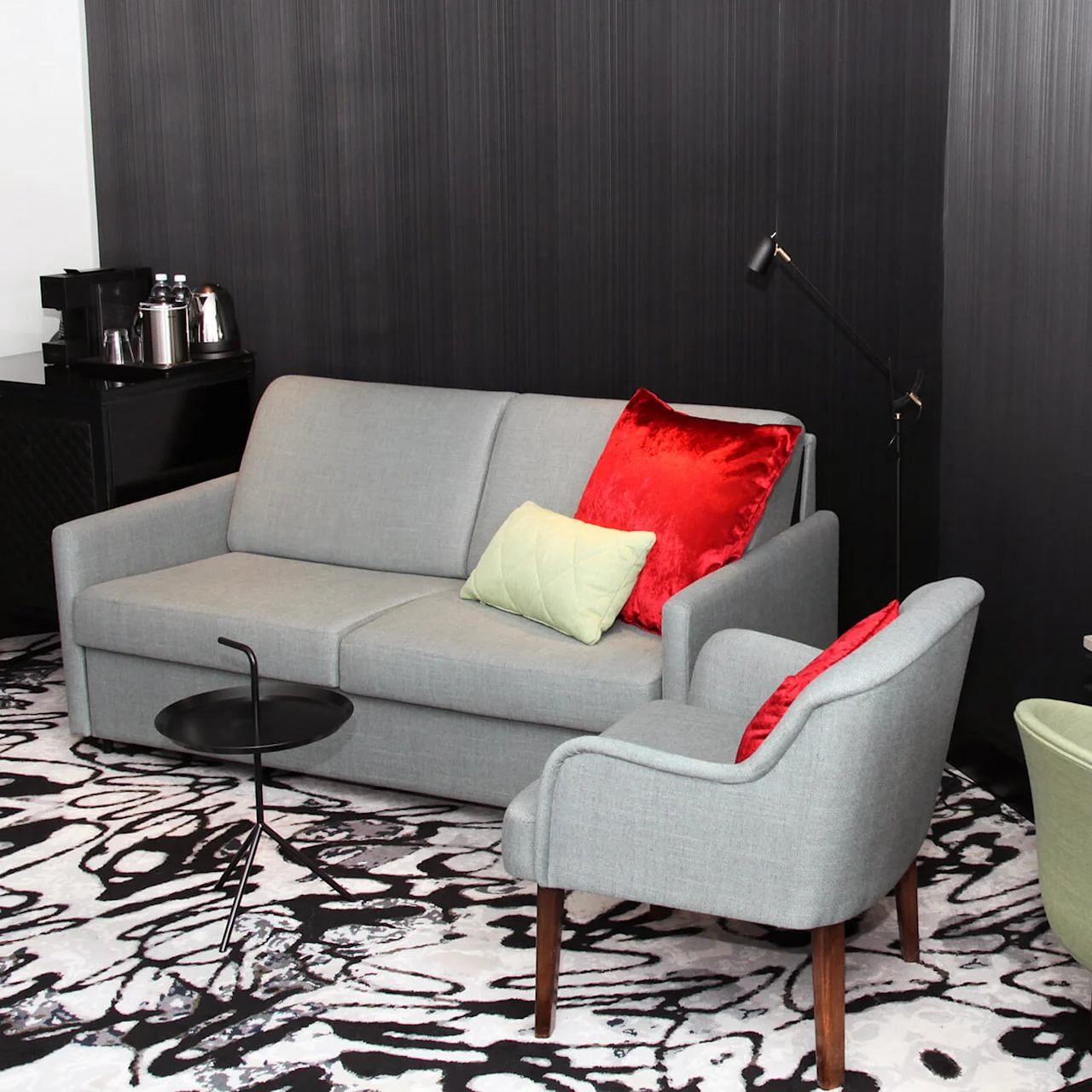 A modern living area with a grey sofa, colored pillows, armchairs, and a flat-screen TV, in a dark-walled room with patterned carpet.