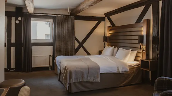 Et hyggeligt hotelværelse med en stor seng, synlige træbjælker og blød belysning, perfekt til et afslappende ophold.