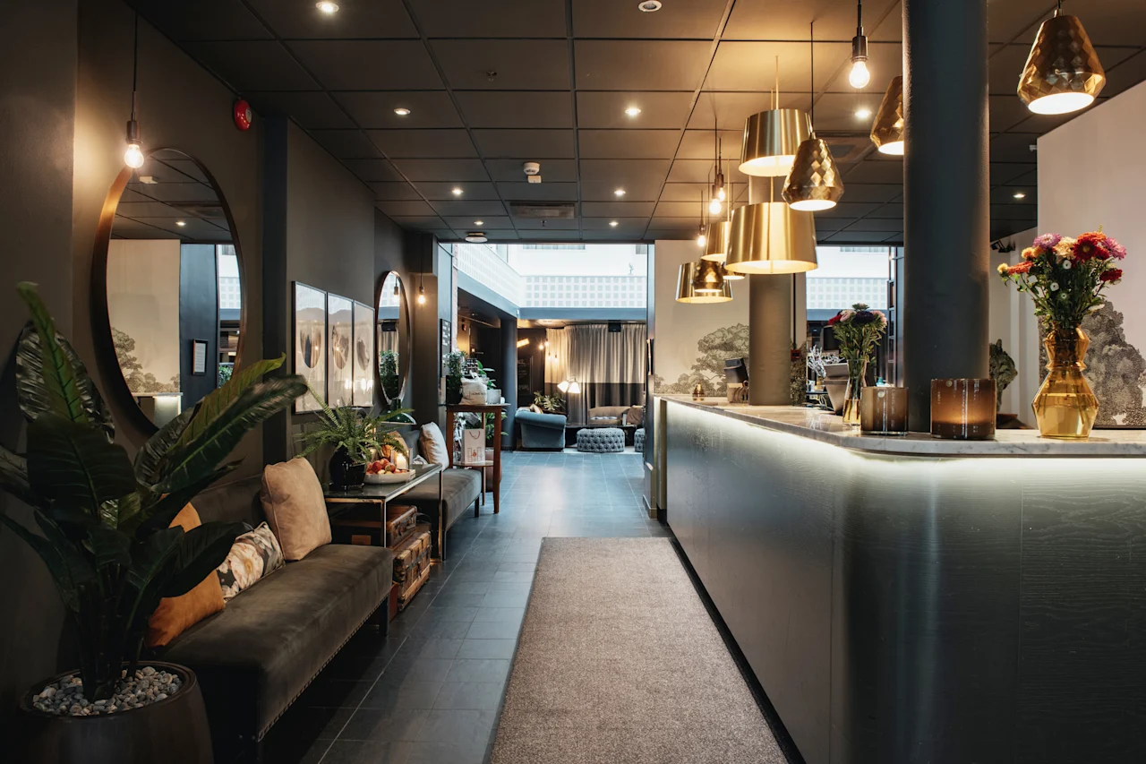 Et indbydende hotelreceptionsområde med en elegant disk, varm belysning og et hyggeligt loungeområde med grønne planter.