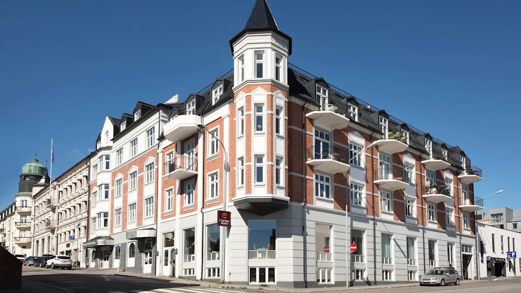 Et hjørnebygg med tårn, balkonger og store vinduer under en klar blå himmel.