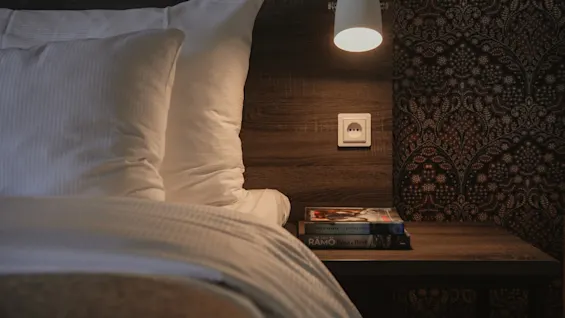 A warm and inviting bedside area at Home Hotel Grand, Helsingborg, featuring a lit lamp, books, and comfortable bedding.