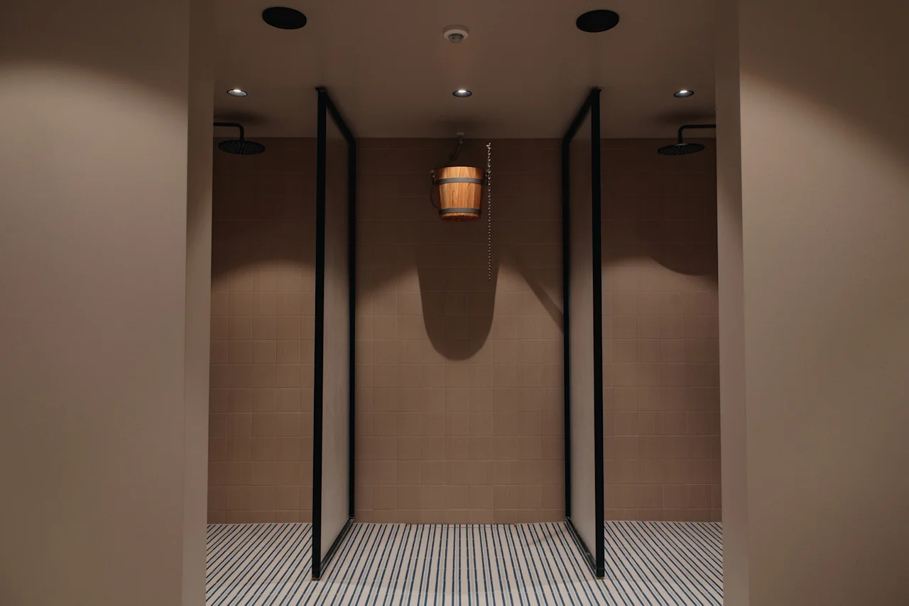 Shower area at Home Hotel Uppsala with two shower stalls and a wooden bucket for a refreshing cold water douse.