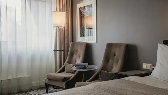 Ett mysigt hotellrum med två fåtöljer, en golvlampa och en säng, som inbjuder till avkoppling och komfort.