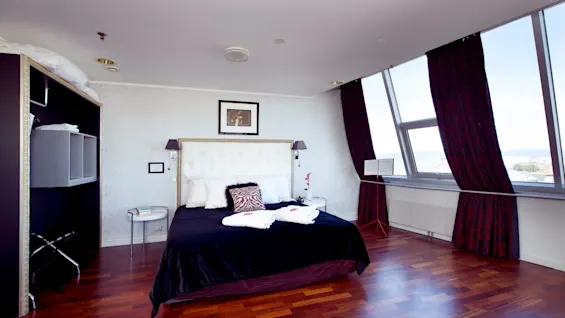 A neatly made bed with pillows and a blanket dominates a luxurious bedroom, featuring large windows offering a panoramic view.