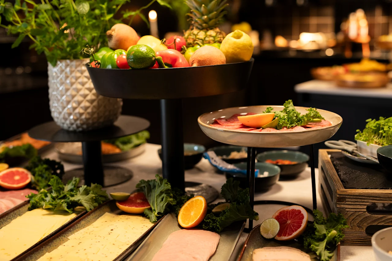 En livlig buffé med frisk frukt, grønnsaker, pålegg og oster på serveringsfat i flere nivåer.