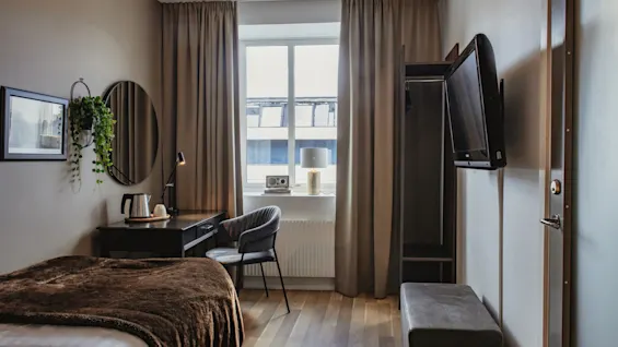 Viihtyisä hotellihuone sängyllä, työpöydällä ja ikkunalla, joka tarjoaa mukavan tilan rentoutumiseen tai työskentelyyn.