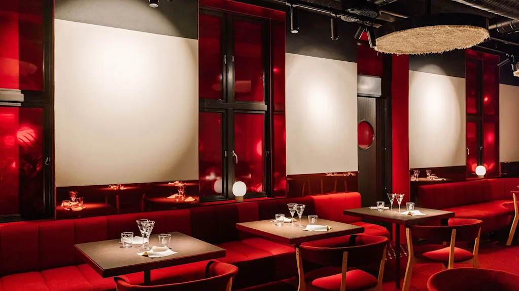 A stylish restaurant interior with plush red booth seating, matching chairs, and dark wooden tables set for dining.
