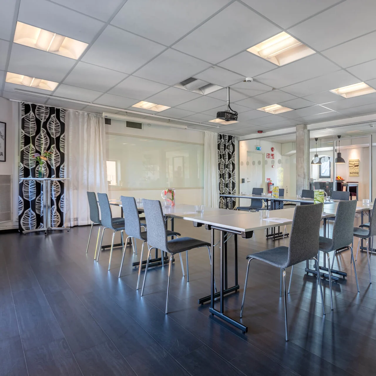 A modern meeting room with a large table and chairs, bright lighting, and a kitchenette in an office setting.