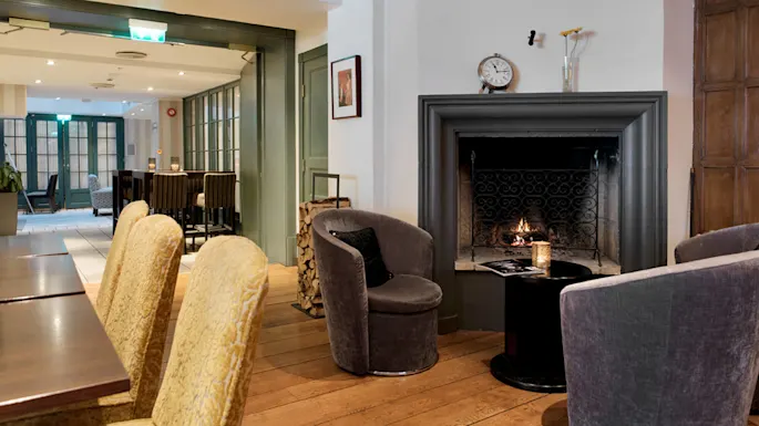 A cozy room with upholstered chairs, a lit fireplace, and a wood floor, in a tranquil, inviting setting.