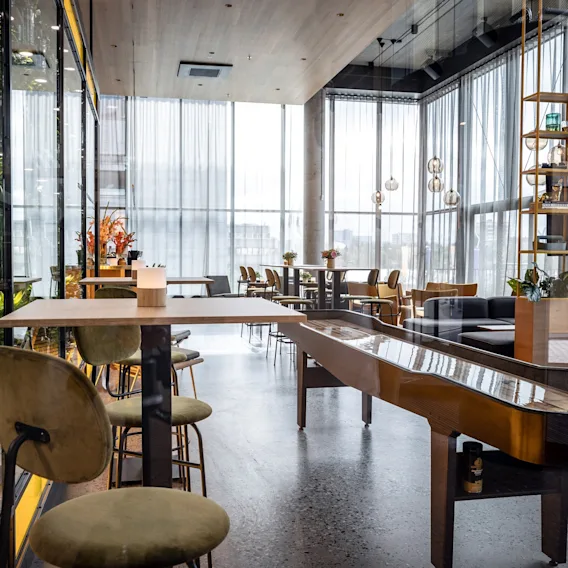 Bord og stoler er arrangert i en moderne, lys kafé med gulv-til-tak-vinduer. Dekorative planter og hyller forbedrer det moderne designet.