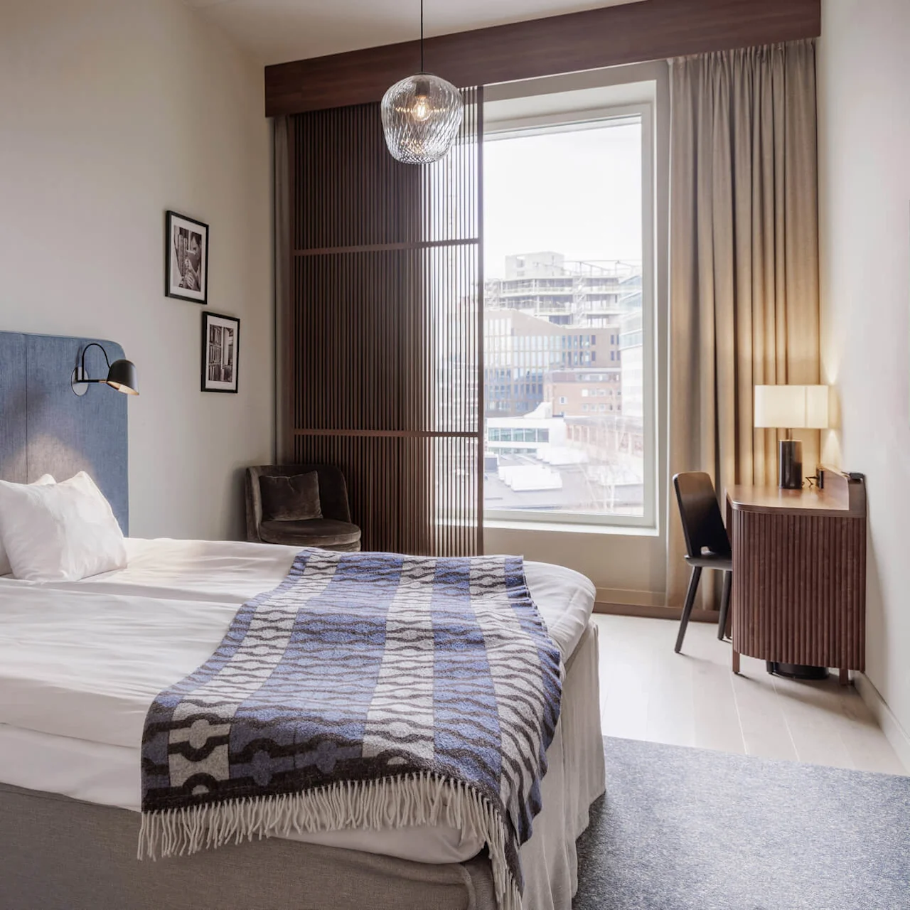 A neatly made bed in a modern hotel room with natural light from a window.