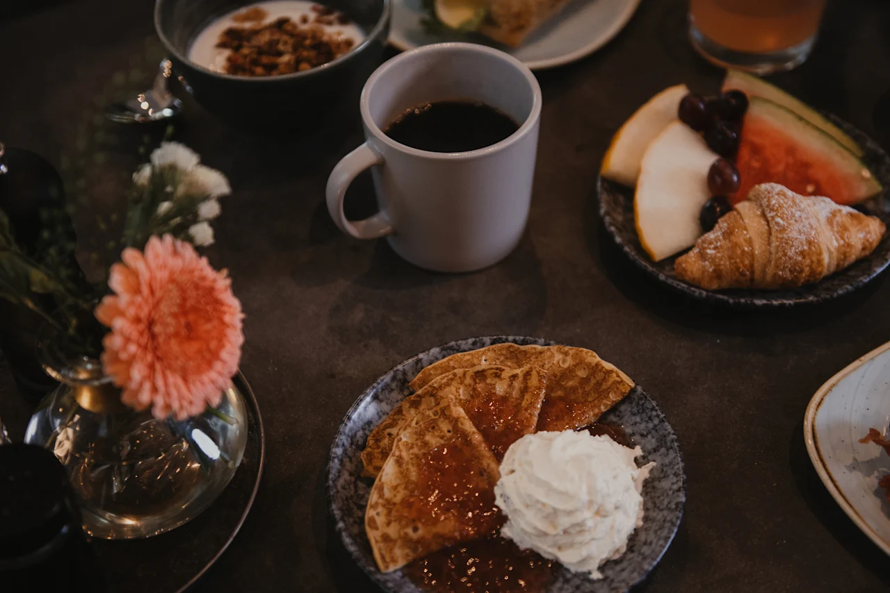 A delicious breakfast spread with coffee, yogurt, fruit, a croissant, and pancakes, enjoyed at Home Hotel Uppsala.