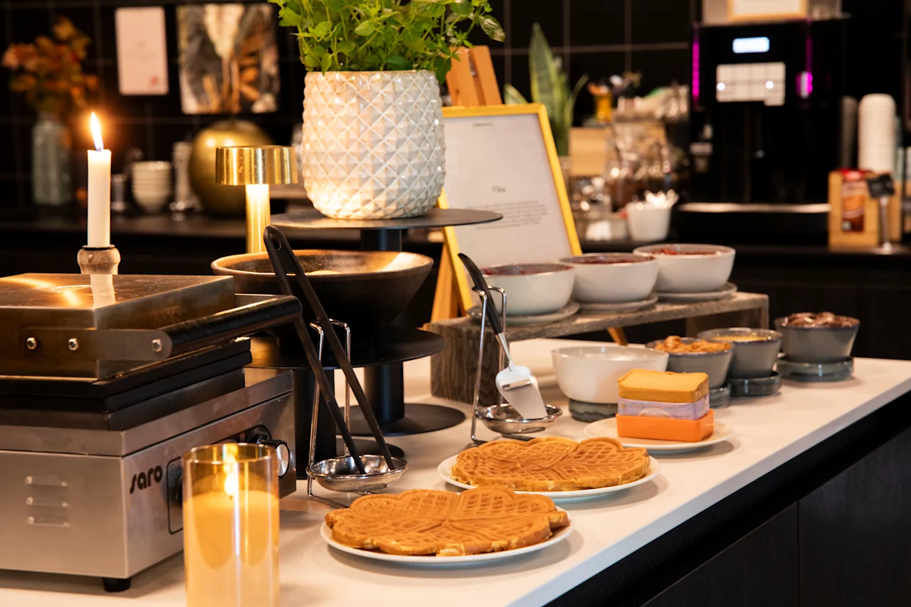 En herlig frokostbuffé med nystekte vafler, diverse pålegg og et vaffeljern, som skaper en koselig og innbydende atmosfære.