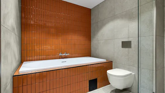Et moderne bad med badekar og livlige oransje fliser, samt et elegant toalett. Stilfullt og innbydende.