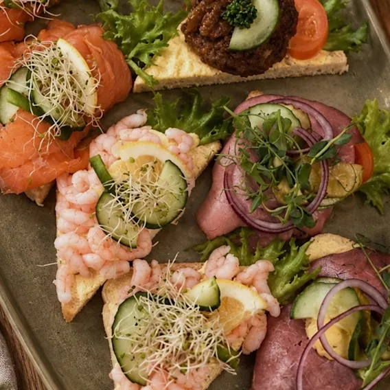 Et fat med snitter pyntet med røkt laks, reker, roastbiff, agurk og friske spirer.