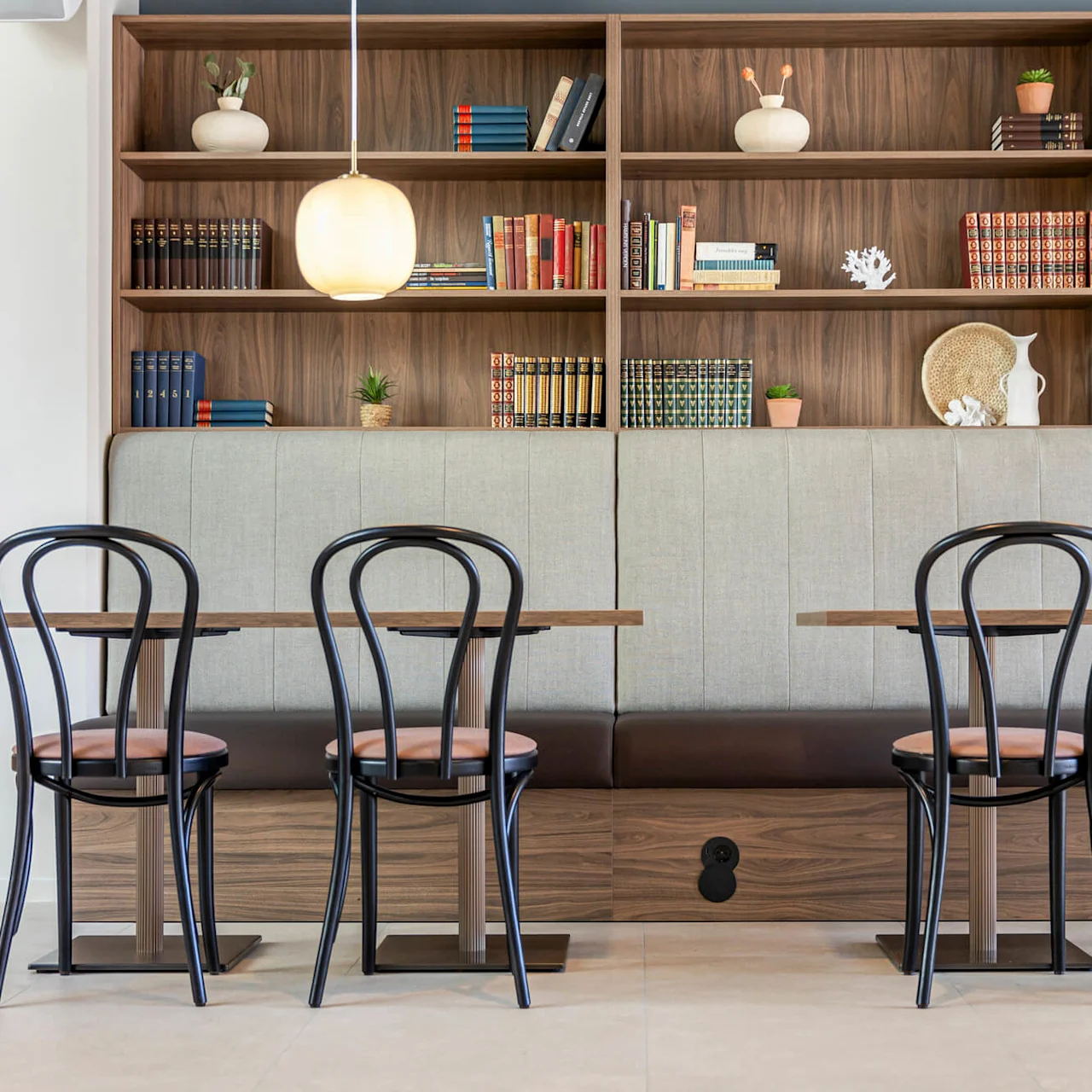 Contemporary chairs facing a wooden shelf with books and decorative items, located in a modern café setting.