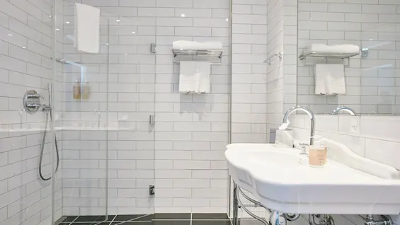 Et rent og moderne badeværelse med glasbruser, hvide fliser, en stilfuld håndvask og friske håndklæder.