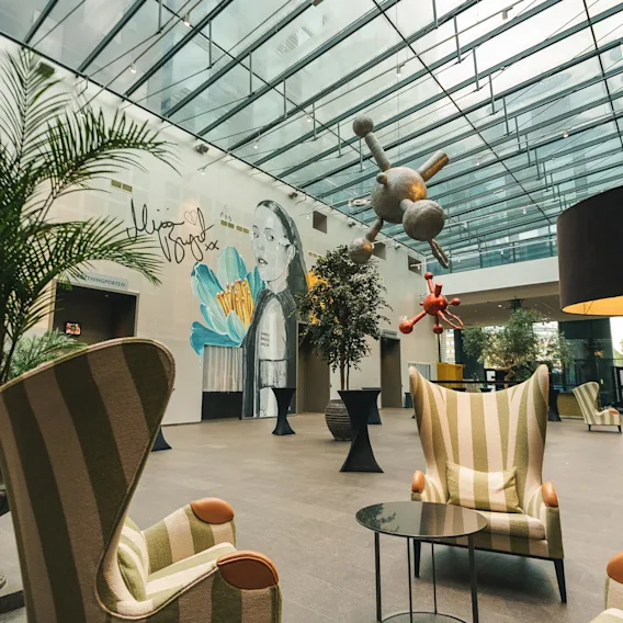 En modern lounge på Clarion Hotel Post med randiga fåtöljer, växter, en väggmålning, abstrakt konst och en "INNGANGSPORTEN"-skylt.