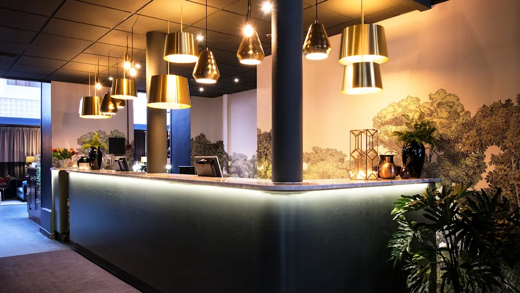 A sleek reception desk with overhead pendant lights in a stylish lobby, featuring decorative plants and a mural.