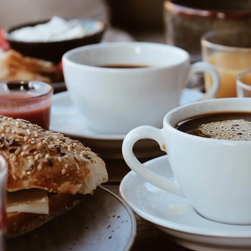 A steaming cup of coffee is the focal point on a table filled with breakfast items including pastries, fruit, and juice.