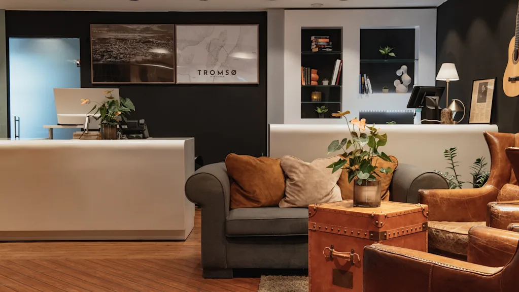 A welcoming hotel lobby featuring a reception desk and a cozy seating area, with 'TROMSO' displayed prominently on the wall.