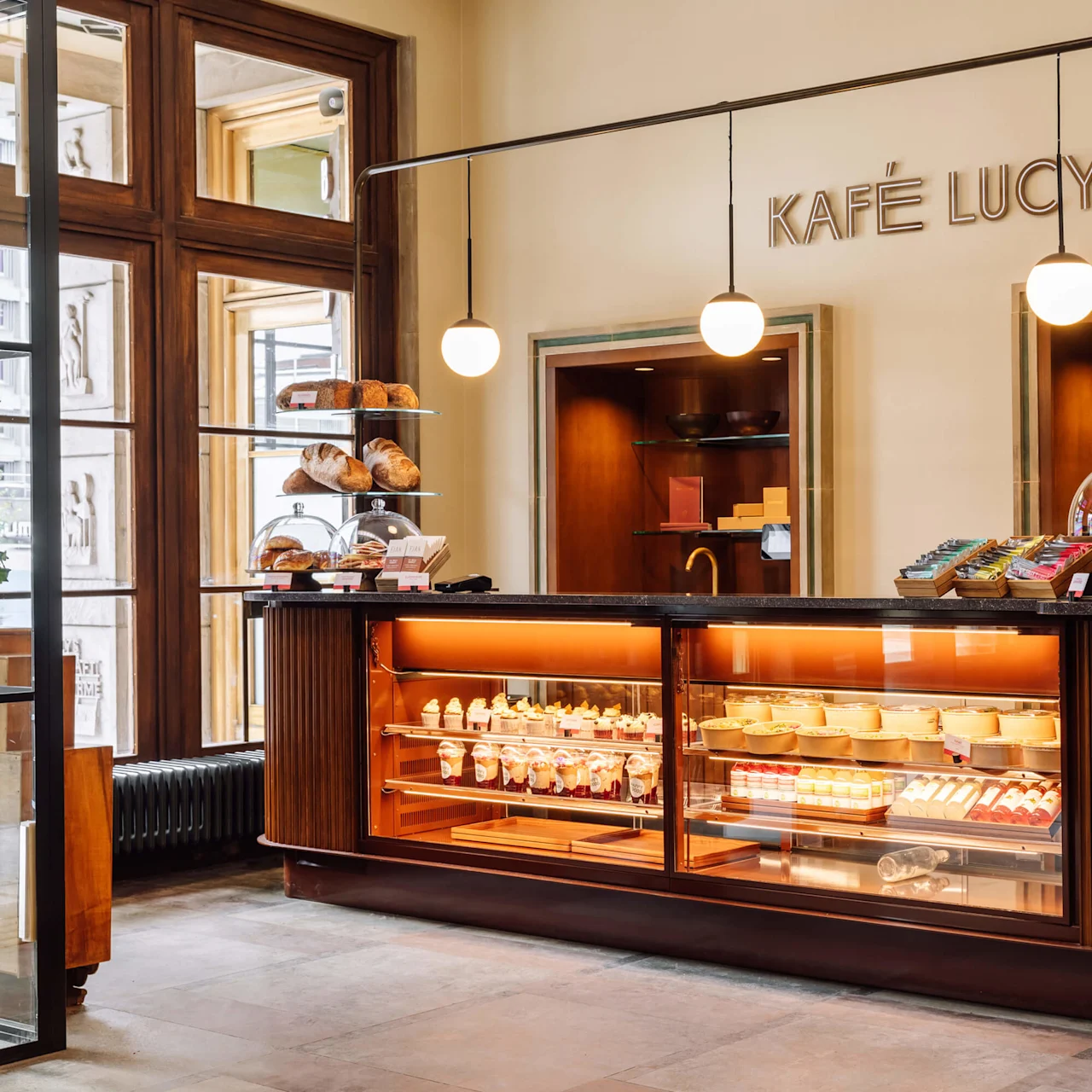 Trædisk i et café fyldt med bagværk, elegant belysning overhead, i et airy rum. Skiltet læser "KAFÉ LUCY".