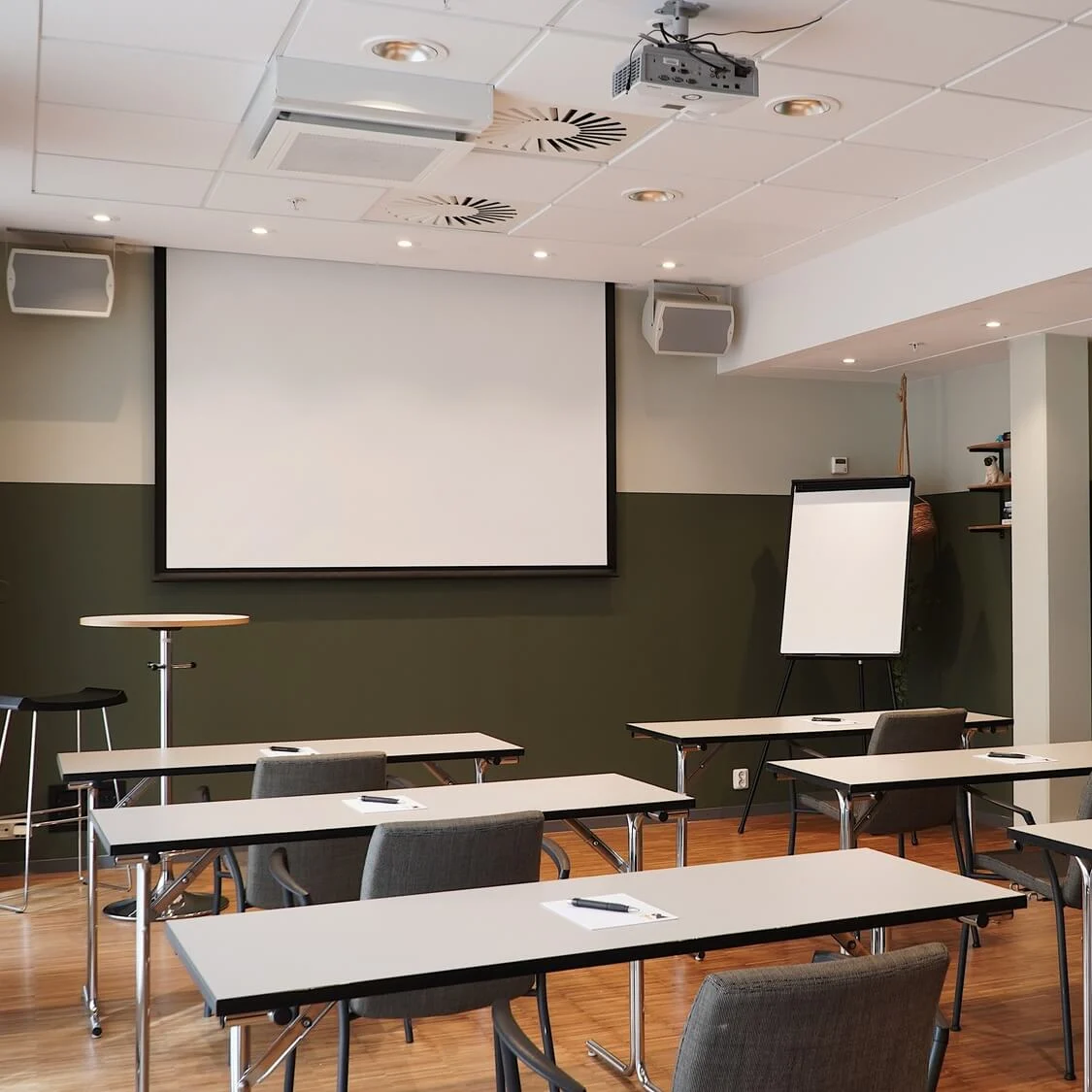 Tables set up in a conference room with empty chairs, a projector, and a screen, awaiting attendees.