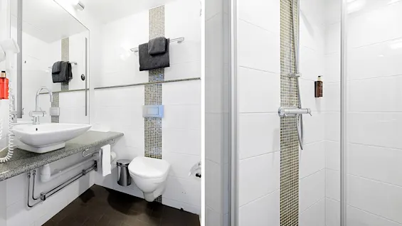 A modern bathroom with a sink, toilet, and shower, tiled in white with mosaic accents.
