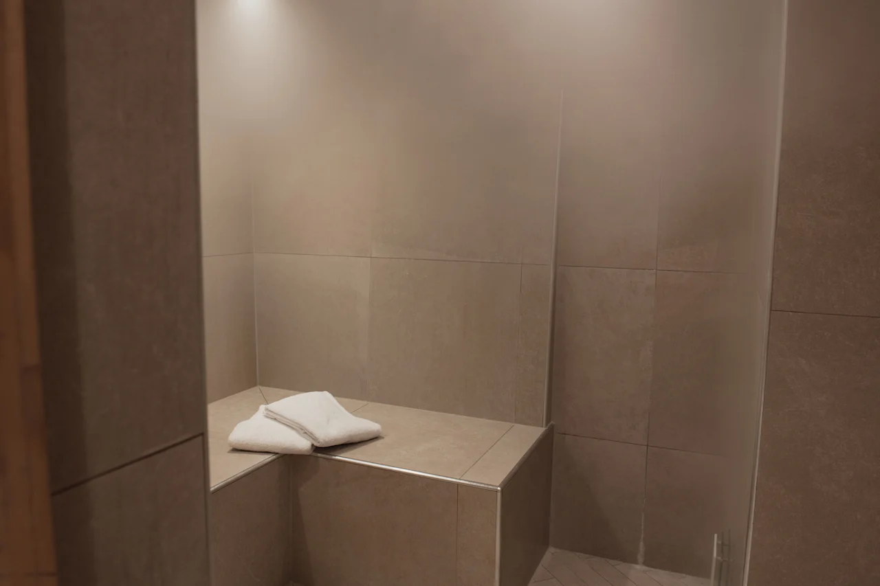 A cozy tiled steam room at Home Hotel Uppsala, featuring a comfortable bench with fresh white towels.