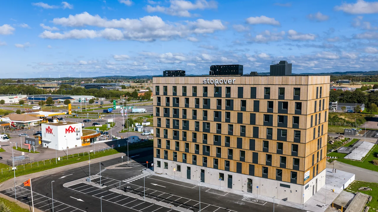 En rektangulär byggnad med flera våningar märkt "Söderöver" står mot en bakgrund av ett förortsområde. I närheten syns en "Max"-snabbmatsrestaurang längs ett gatunät.