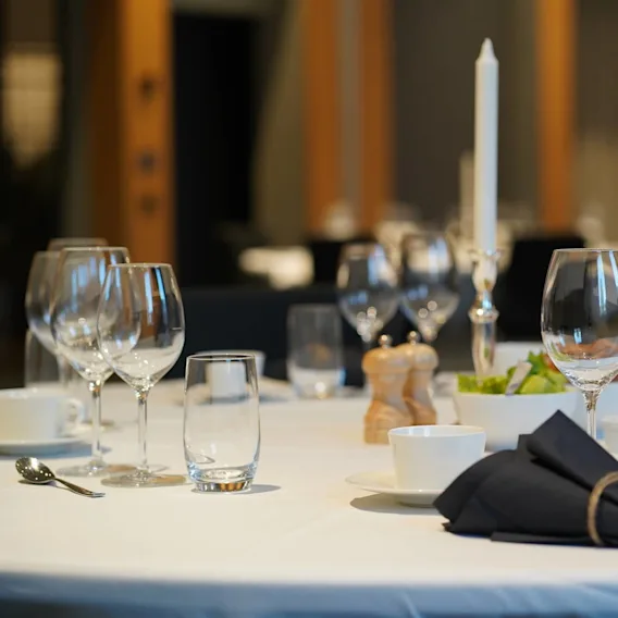 A round dining table set elegantly with glassware and napkins, surrounding a central candle, in a formal dining setting with soft lighting.