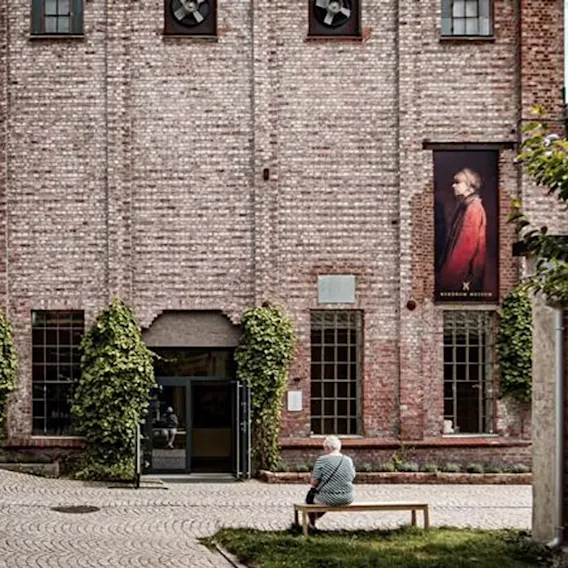 En person sitter på en benk utenfor en mursteinsbygning med et stort portrettbanner.