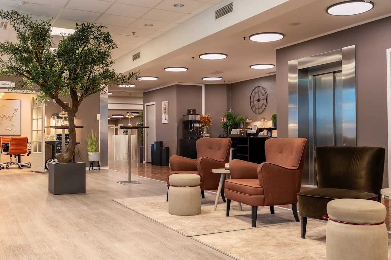 Kutsuva hotelliaula mukavilla istuimilla, suurella ruukkupuulla ja hissillä, luoden rennon tunnelman.