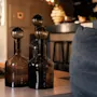 Tre dekorative glasflasker med sfæriske propper på et bord i et blødt oplyst interiør, der skaber en hyggelig atmosfære.