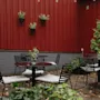 A cozy outdoor seating area with black tables and chairs against a red wooden wall, adorned with plants and fallen leaves. Home Hotel Kung Oscar.