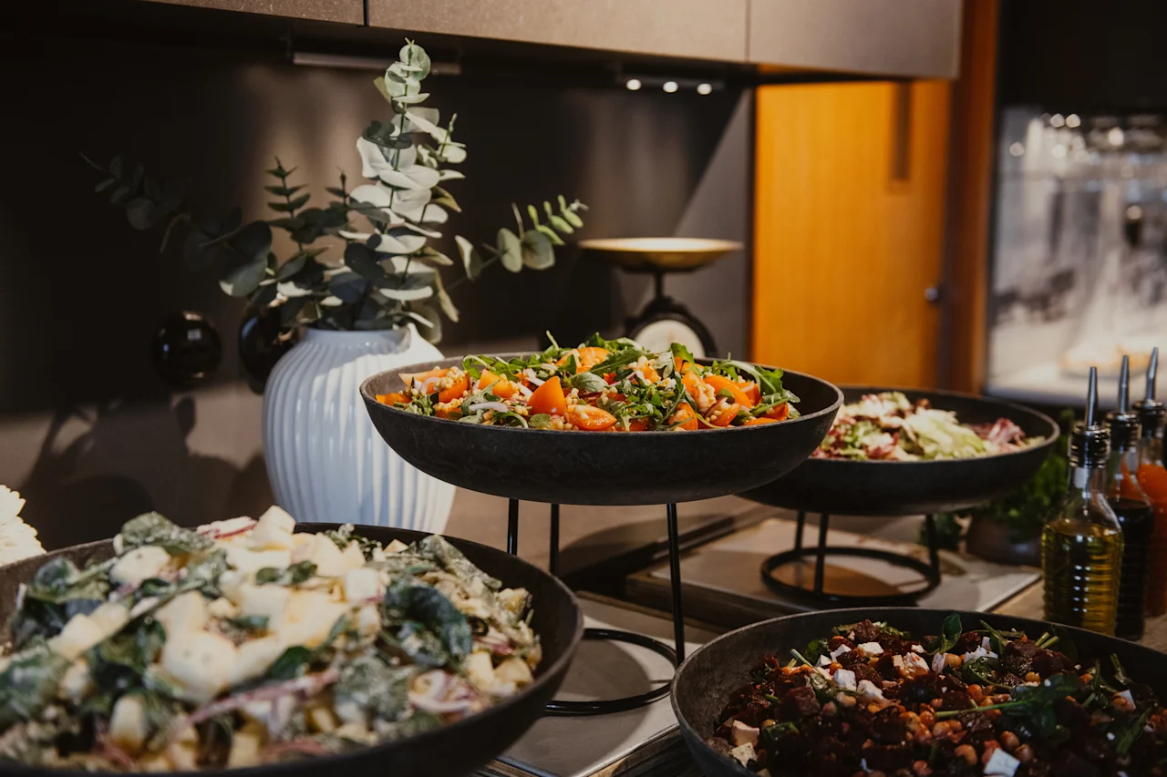 Eloisa buffet, jossa on erilaisia tuoreita salaatteja tummissa kulhoissa, taustalla koristekasvi.