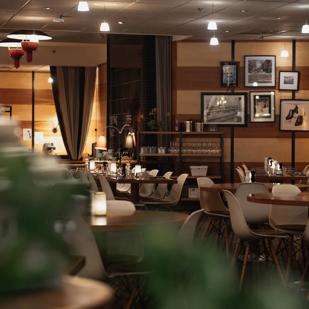 Cozy restaurant with wooden tables and white chairs, set for dining. Warm lighting and framed pictures on the wall create an inviting ambiance.