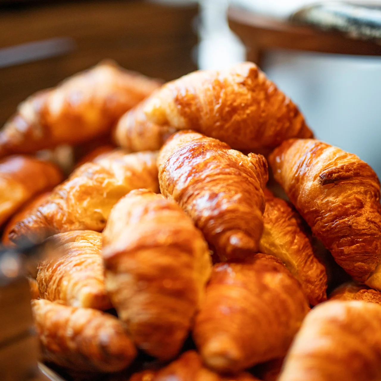 Croissanter stables på en tallerken, med en gyllen og sprø tekstur. De er plassert i en koselig setting med en uskarp bakgrunn, som antyder et kafé eller bakeri.